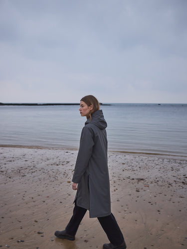 Person walking on a beach with a gray  Tanta Rainwear coat
