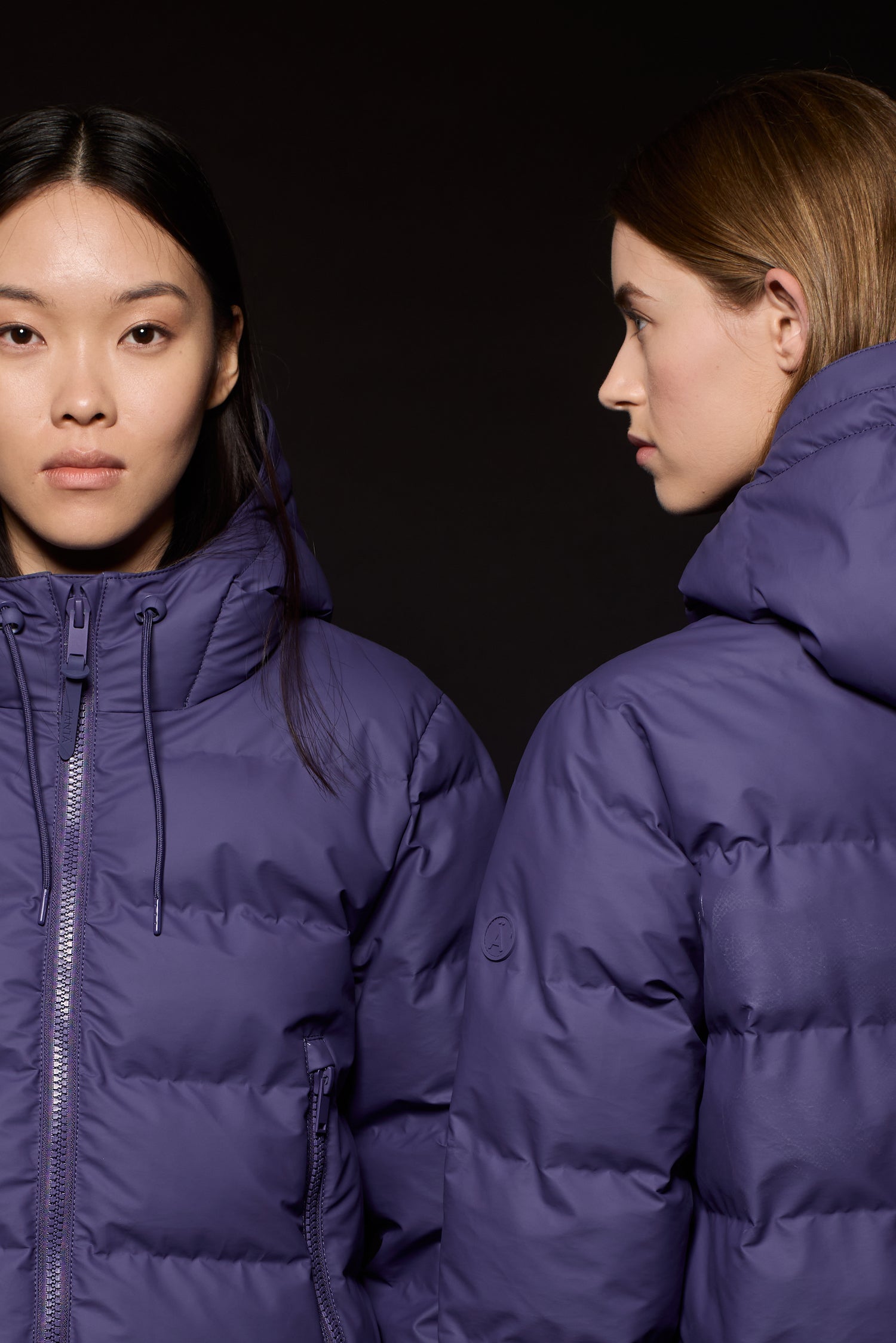 Two people wearing purple puffer jackets from Tanta Rainwear against a black background