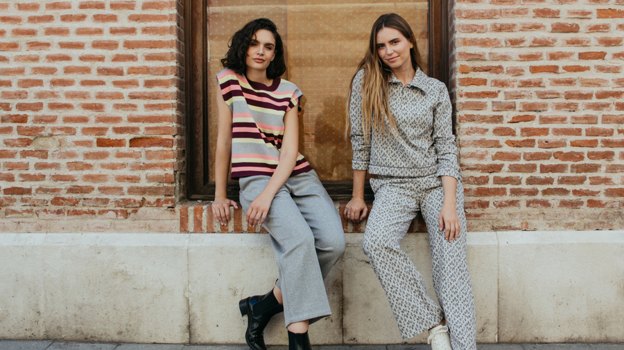 Two women sitting against a brick wall, wearing stylish outfits from MD'M