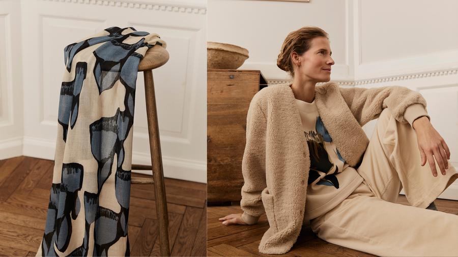 Woman wearing a beige Masai sweater and skirt with a blue and white patterned blouse, sitting in a room.