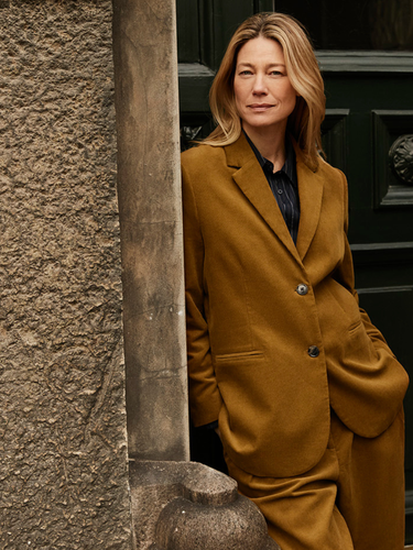 Woman in a mustard suit from Masai standing against a textured wall and black door.