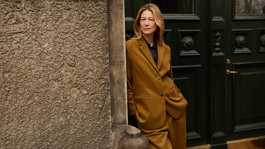 Woman in a mustard suit from Masai standing against a textured wall and black door.