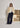 Woman wearing a beige teddy jacket and navy pants from Peppercorn standing in front of framed artwork.