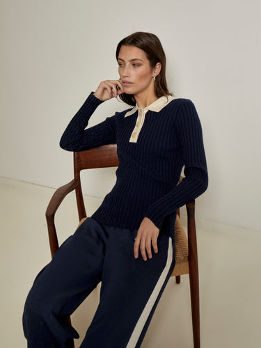 Woman sitting on a chair wearing a dark blue ribbed sweater with a white collar and matching pants from the Peppercorn Fall Winter collection.