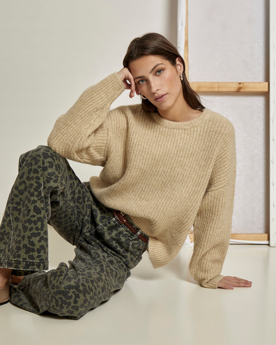 Woman wearing a beige sweater and leopard print pants from Peppercorn sitting on the floor.