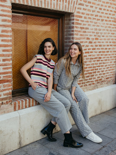 Two young women sitting on a ledge against a brick wall wearing stylish Fall outfits from MD'M